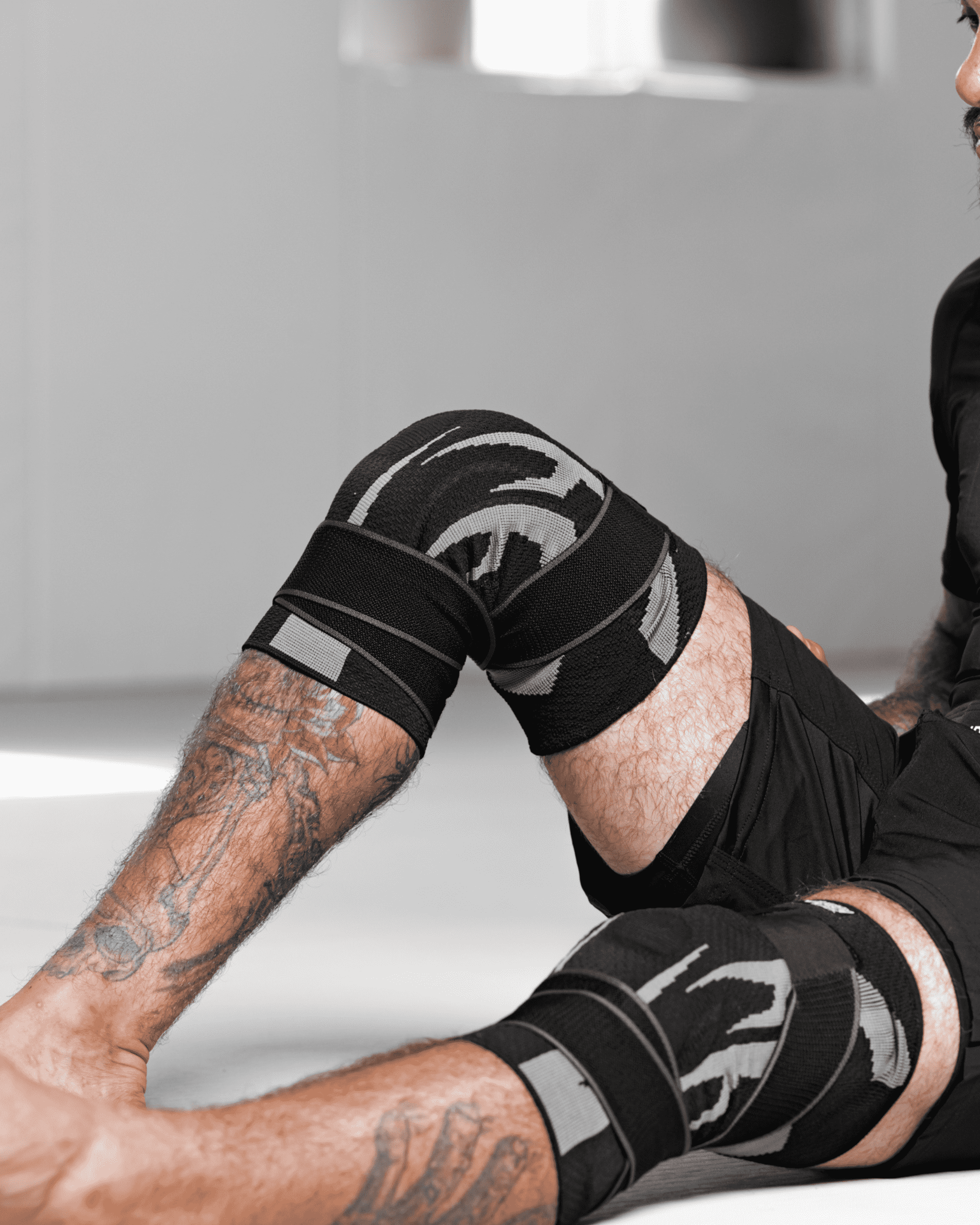 Man in rash guard and knee brace kneeling and looking at the camera.